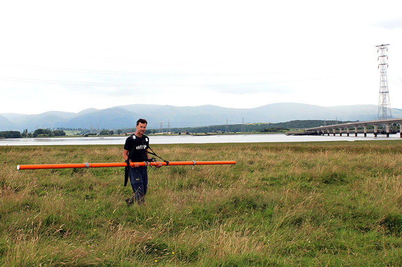 Man holding long horizontal orange pole in field of long grass